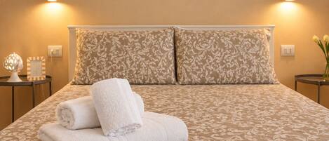 A neatly made bed with a patterned bedspread, two pillows, and folded towels.