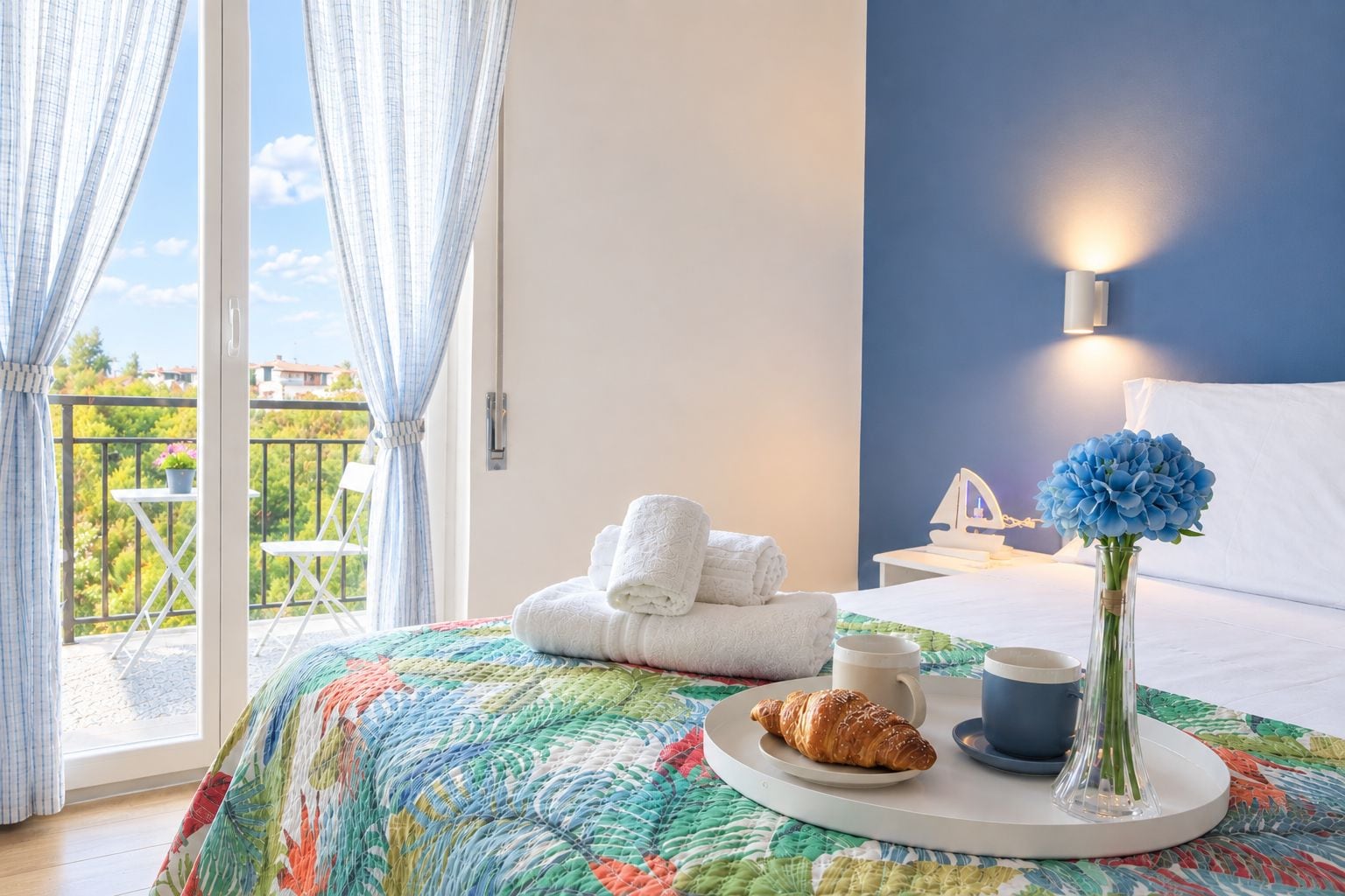 A bedroom with a bed, a bedside table with a lamp, a window with curtains, and a balcony with a chair and table.