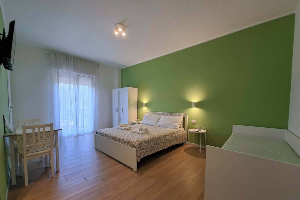 Un dormitorio con cama, una silla, un armario, una mesita de noche y una pequeña mesa con lámpara.