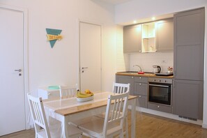 Una cocina compacta con una mesa de madera, sillas blancas y un frutero.