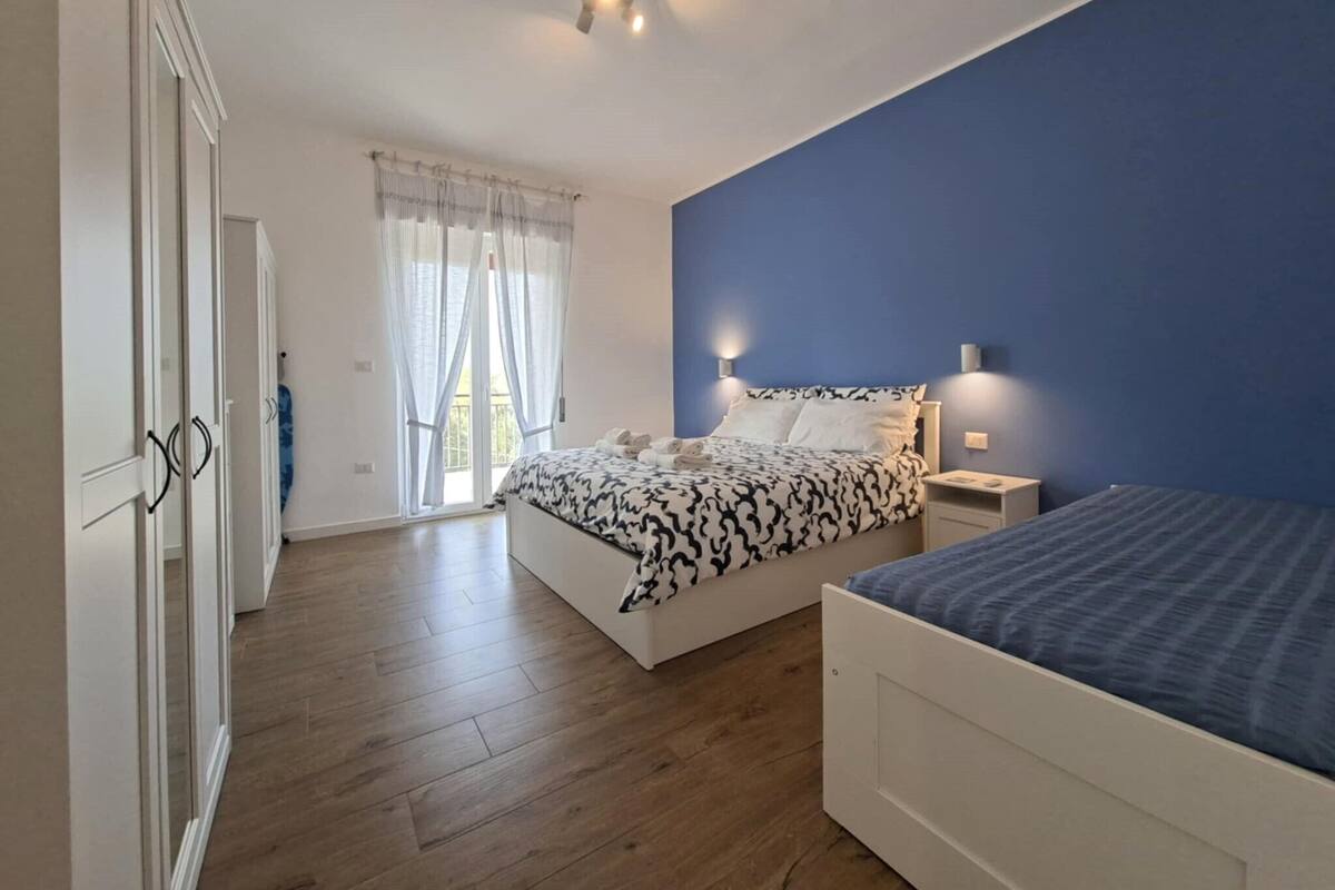 Un dormitorio con cama, armario, mesita de noche y ventana con cortinas.