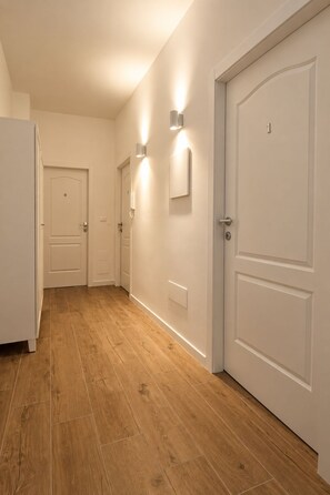 Un pasillo con piso de madera, puertas blancas e iluminación empotrada.