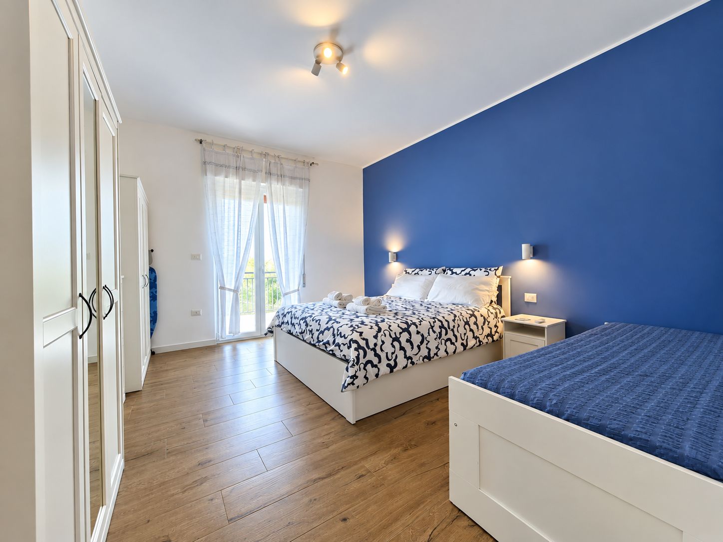 A bedroom with a bed, a nightstand, a wardrobe, and a window with curtains.