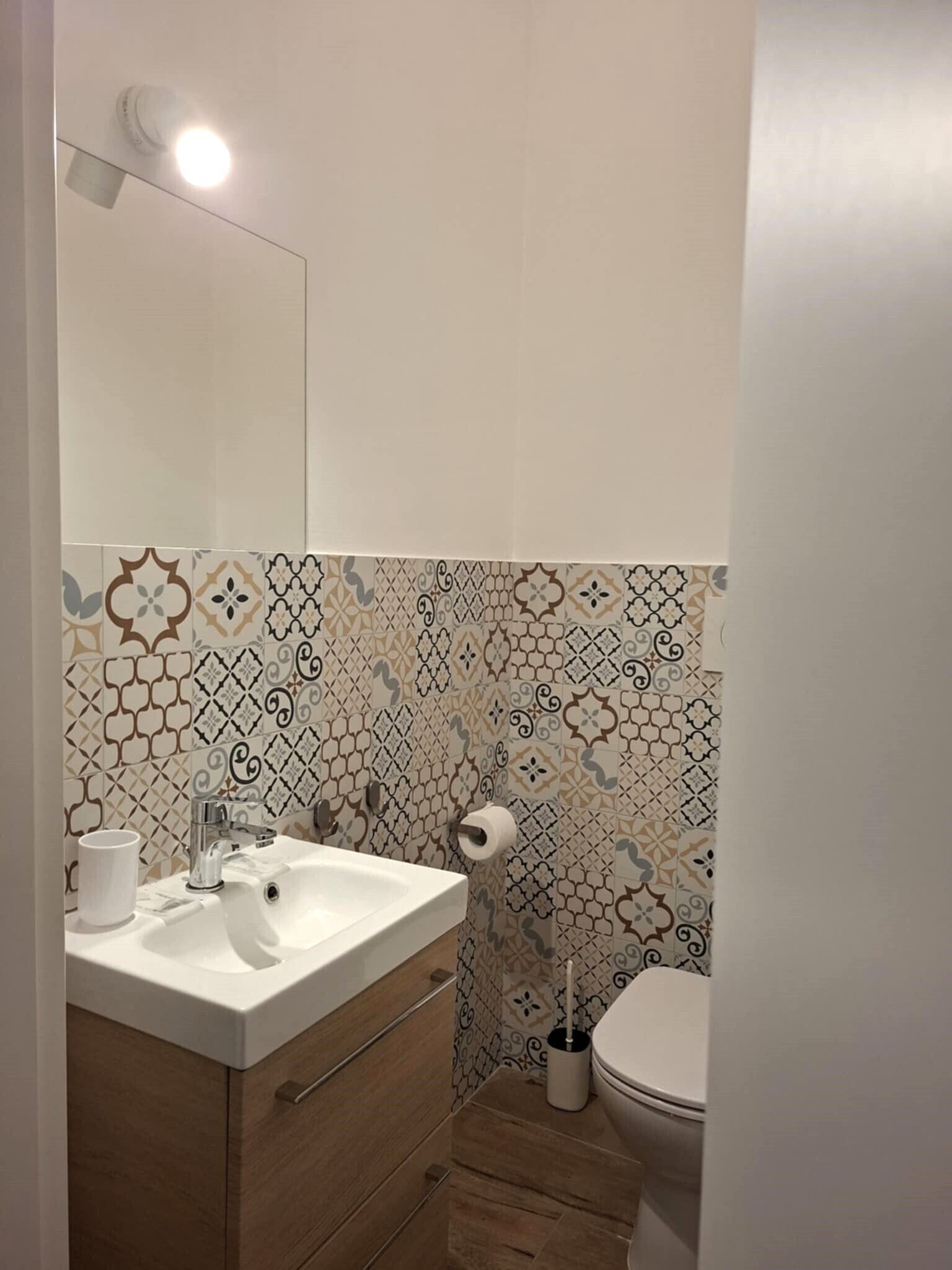 A bathroom with a white sink, a mirror, a toilet, and patterned tiles.