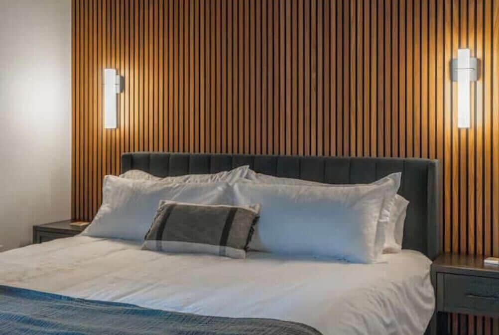 Een hotelkamer met een wand van houten latten, een groot bed met witte beddengoed en twee wandlampen.