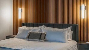 Hotellihuone, jossa on puusäleistä tehty seinä, suuri sänky valkoisilla vuodevaatteilla ja kaksi seinälle asennettua valaisinta.