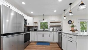 Una cocina moderna con electrodomésticos de acero inoxidable, armarios blancos e iluminación colgante.