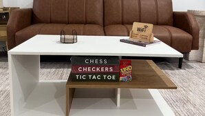 Un salon moderne avec un canapé en cuir marron, une table basse blanche agrémentée d’un détail en bois, et deux tableaux abstraits accrochés au mur.