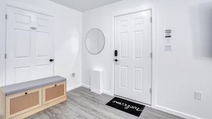 Un couloir avec des portes blanches, un banc, un miroir et un paillasson.