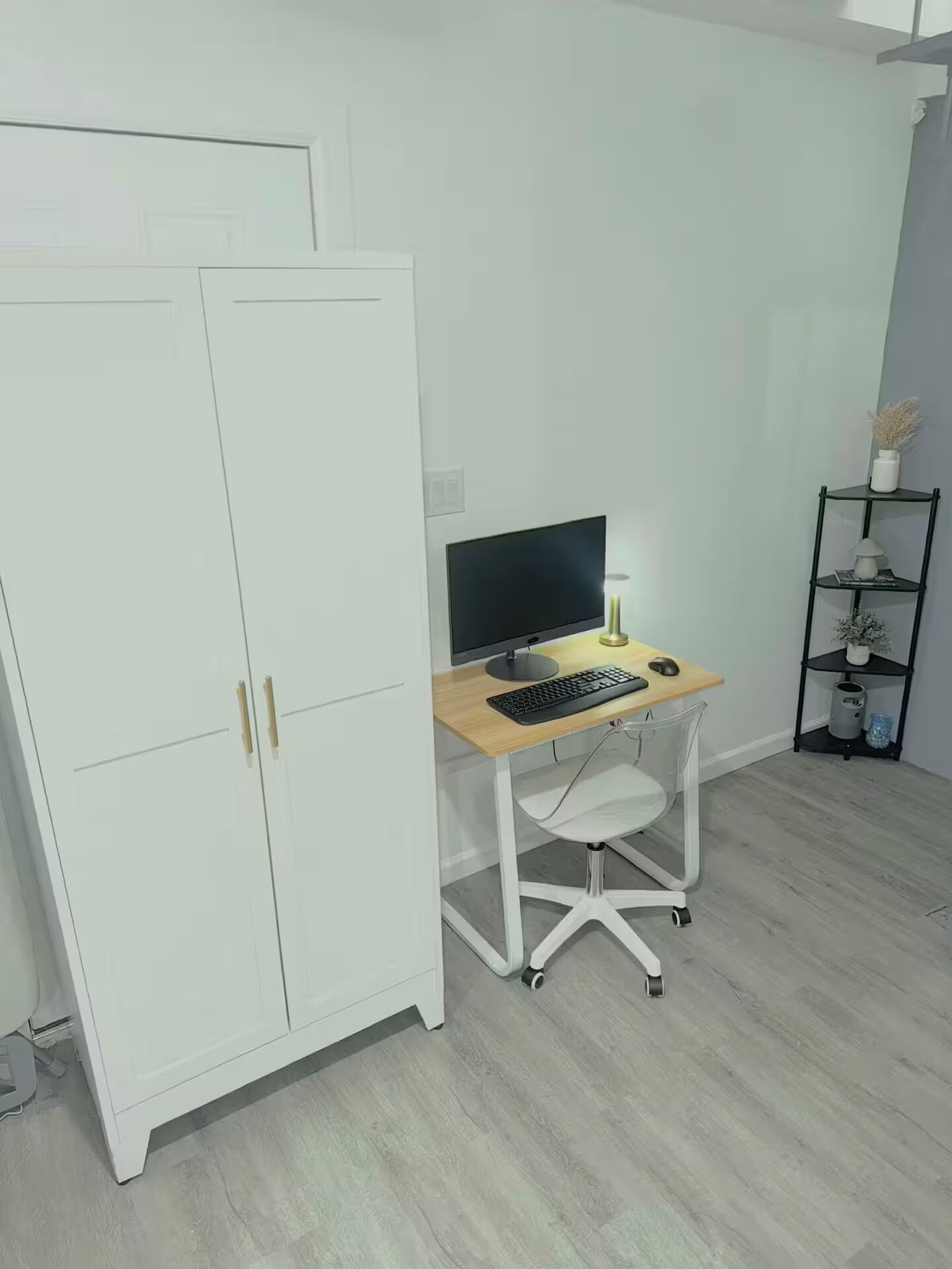 A room with a white wardrobe, a desk with a computer, and a small shelf with decorative items.