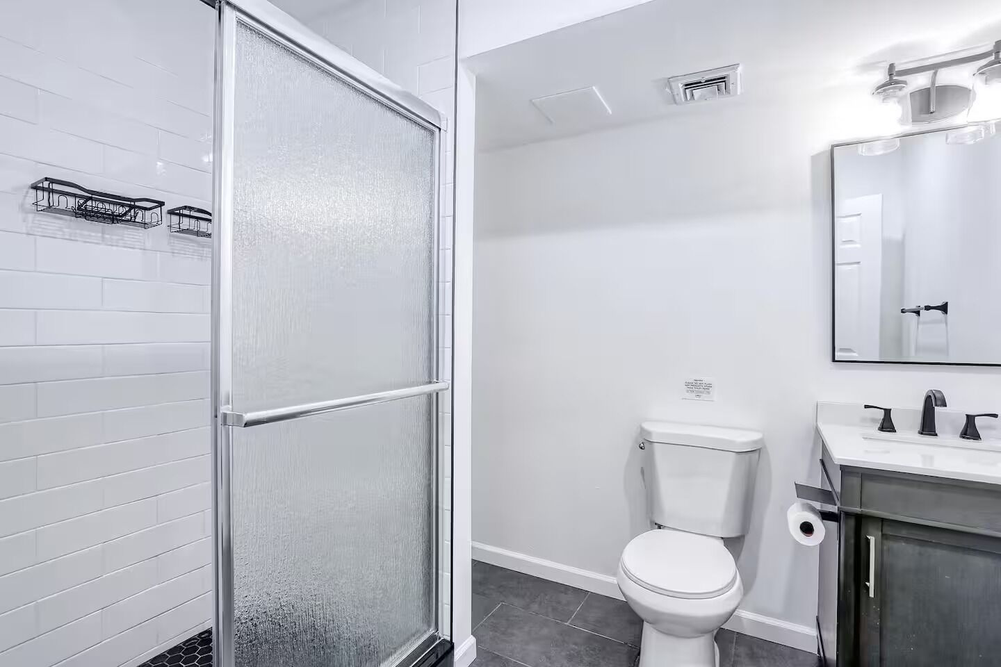 Un bany modern amb una cabina de dutxa de vidre, un vàter blanc i un lavabo amb mirall.