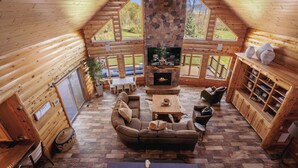 A cozy log cabin interior with a stone fireplace, wooden furniture, and large windows offering views of the outdoors. - NorthLong Lake/Hot Tub, Sandy Beach (Brainerd)