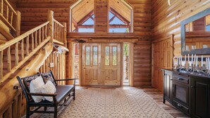 A log cabin interior with a wooden staircase, a bench with a blanket, a large wooden door, and a cabinet. - NorthLong Lake/Hot Tub, Sandy Beach (Brainerd)