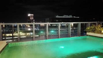 A rooftop pool with a view of city buildings at night.