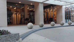 Ingresso di un edificio moderno con ampie porte in vetro, un viale curvo ed elementi decorativi sferici.