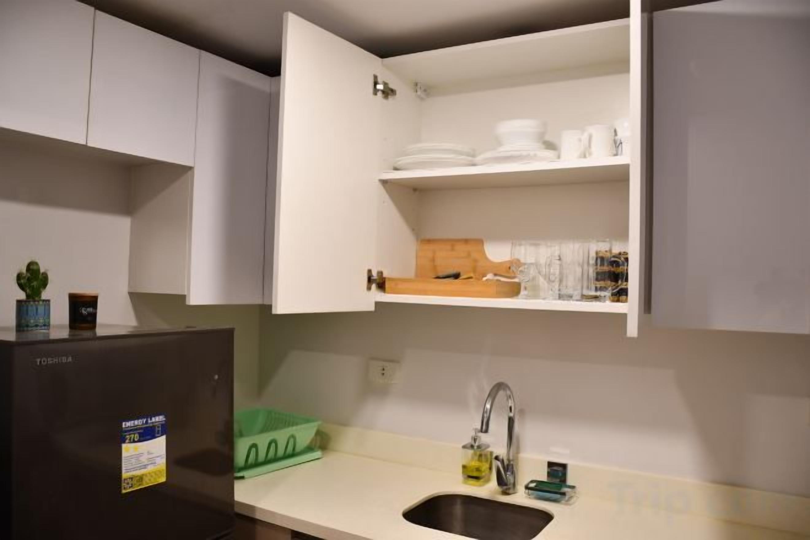 A compact kitchen with a built-in refrigerator, a sink, and upper cabinets with dishes and utensils.