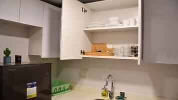 A compact kitchen with a built-in refrigerator, a sink, and upper cabinets with dishes and utensils.