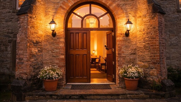 A stone building with a large arched entrance, a prominent window, and two wall-mounted lights. - Historic Barmeath Castle Guest Wing — Luxury Stay Amid Gardens & Woodland (Dunleer)