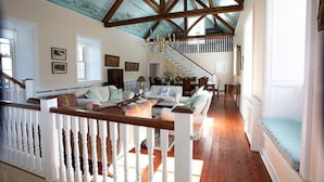 A spacious living room with a high ceiling, wooden beams, a staircase, and a large window. - Historic Barmeath Castle Guest Wing — Luxury Stay Amid Gardens & Woodland (Dunleer)