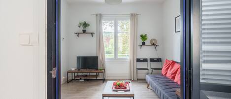 A modern living room with a sofa, a coffee table with fruit, a TV, and a window with curtains.