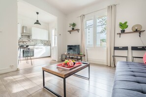 A modern living room with a sofa, a coffee table with fruit, a TV, and a kitchen in the background.