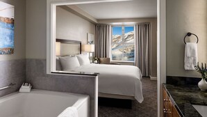A hotel room with a large bed, a bathroom with a bathtub, and a view of snowy mountains through the window.