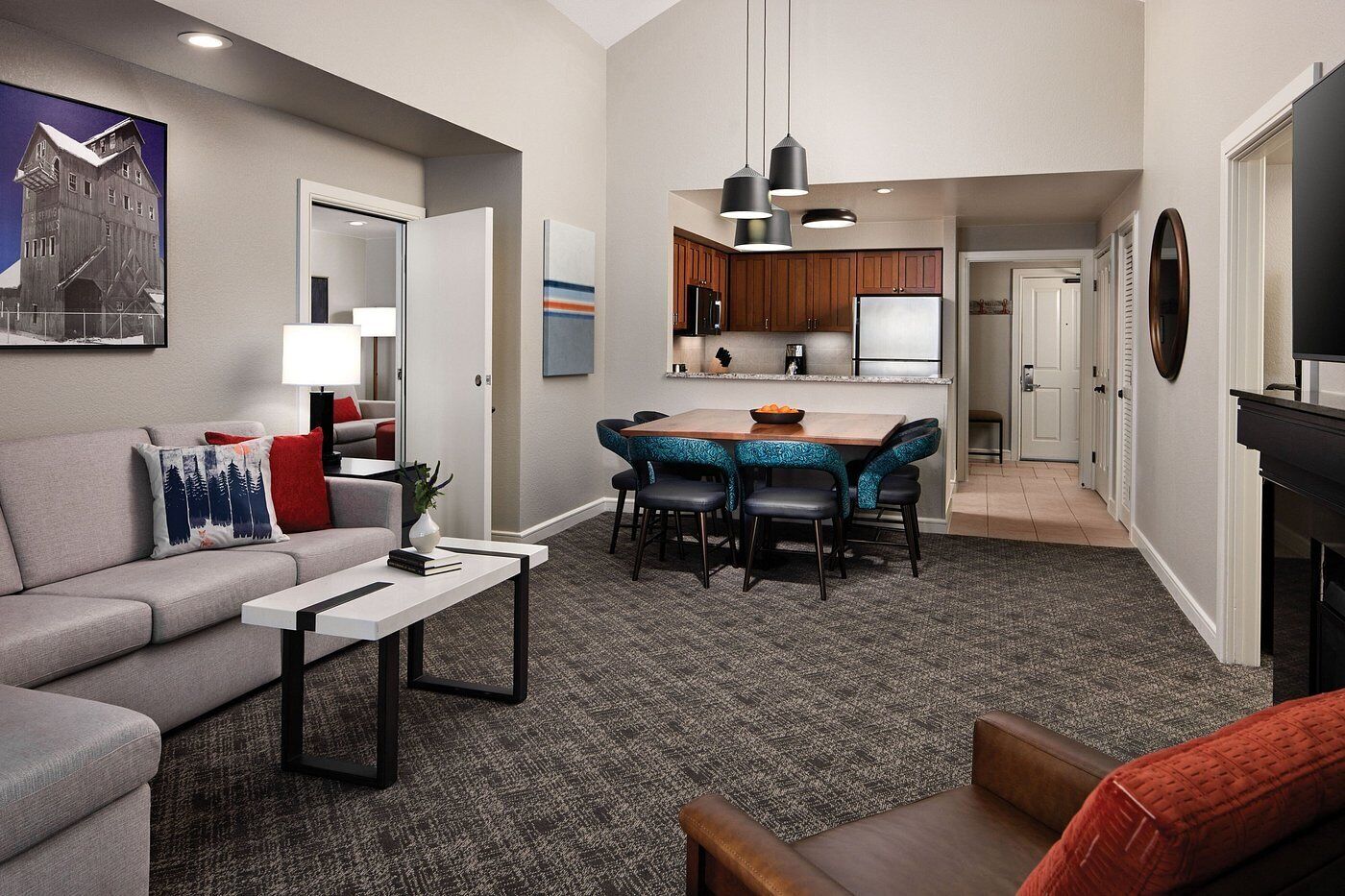 A modern living room with a gray sofa, a coffee table, and a dining area with blue upholstered chairs.