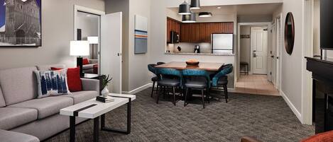 A modern living room with a gray sofa, a coffee table, and a dining area with blue upholstered chairs.
