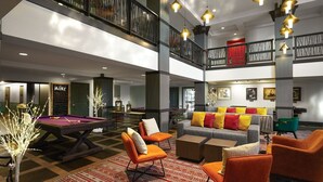 A spacious lobby with a pool table, comfortable seating, and a high ceiling with hanging lights.