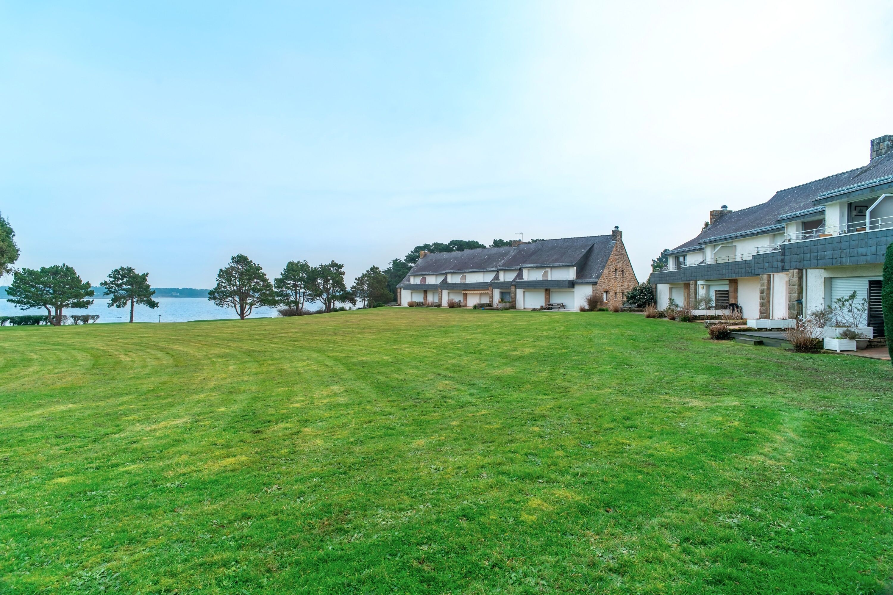 A large, open grassy area with a view of a lake and two houses.
