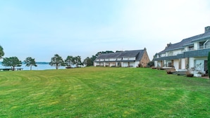 Une vaste étendue d’herbe, dégagée et ouverte, d’où l’on peut admirer un lac et deux maisons.