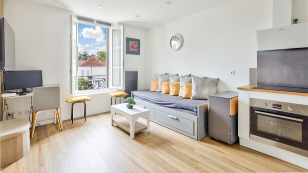 A modern, compact living space with a kitchenette, a dining area, and a sofa with cushions.