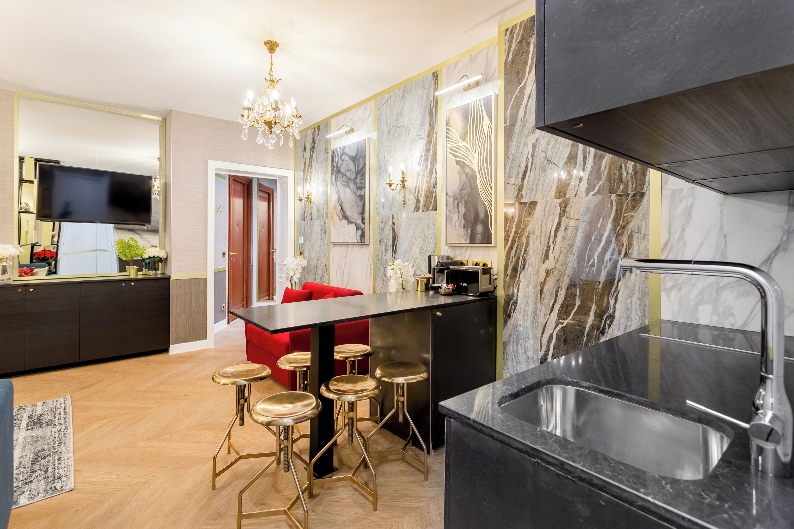 Een moderne keuken met een zwart aanrecht, een roestvrijstalen spoelbak en goudkleurige barstoelen.
