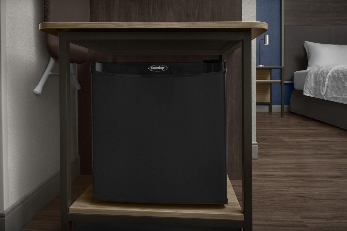 A compact, dark-colored refrigerator in a modern kitchen with a wooden countertop and a built-in shelf.