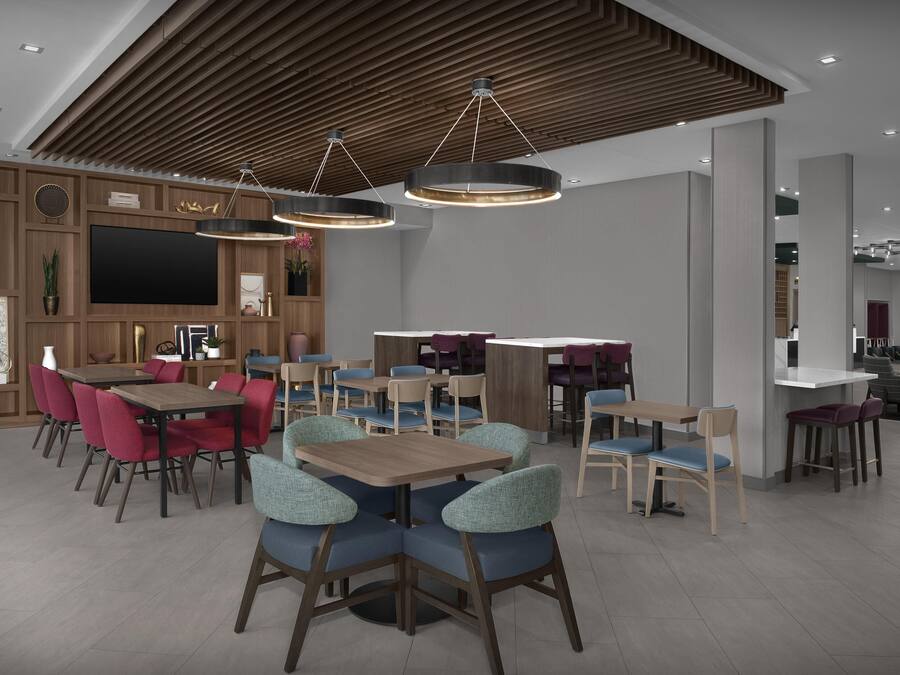 Un espace repas moderne avec des tables et des chaises en bois, un grand téléviseur à écran plat et un éclairage suspendu.