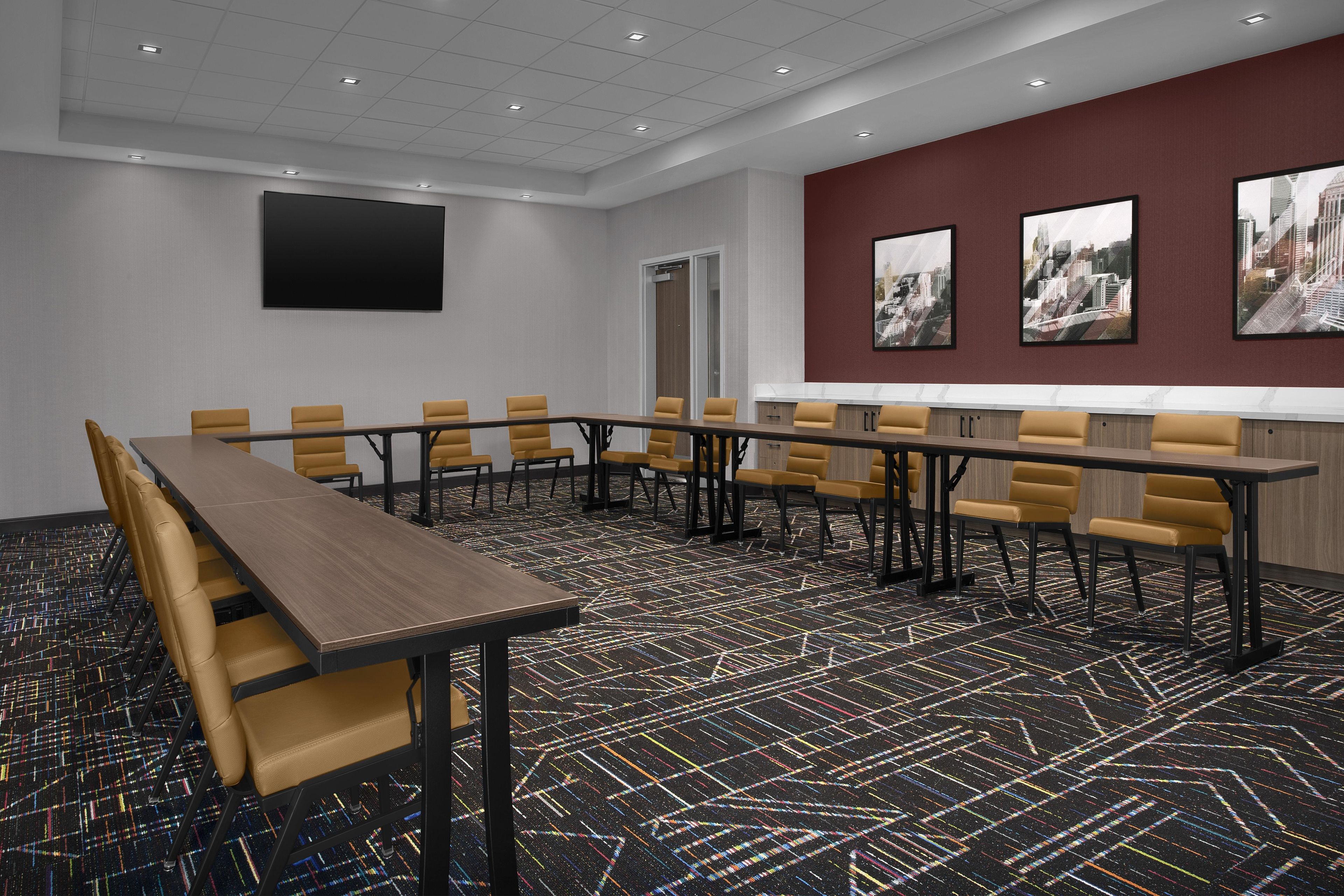 Une salle de conférence avec une longue table, de nombreuses chaises, un grand écran et des œuvres d’art représentant des paysages urbains accrochées aux murs.