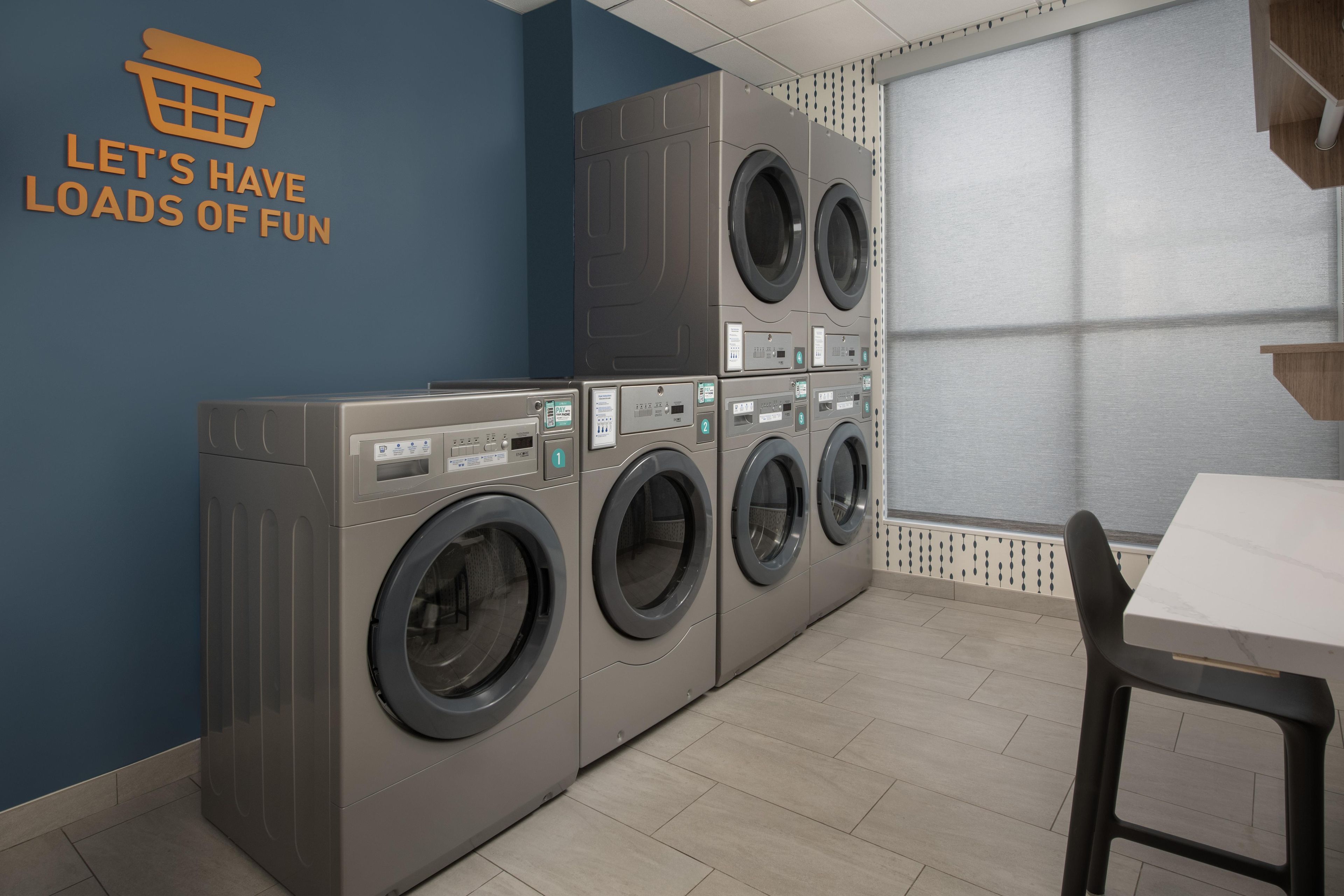Une buanderie équipée de plusieurs machines à laver, d’un sèche-linge fixé au mur et d’une table avec des chaises.