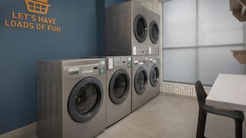 Une buanderie équipée de plusieurs machines à laver, d’un sèche-linge fixé au mur et d’une table avec des chaises.