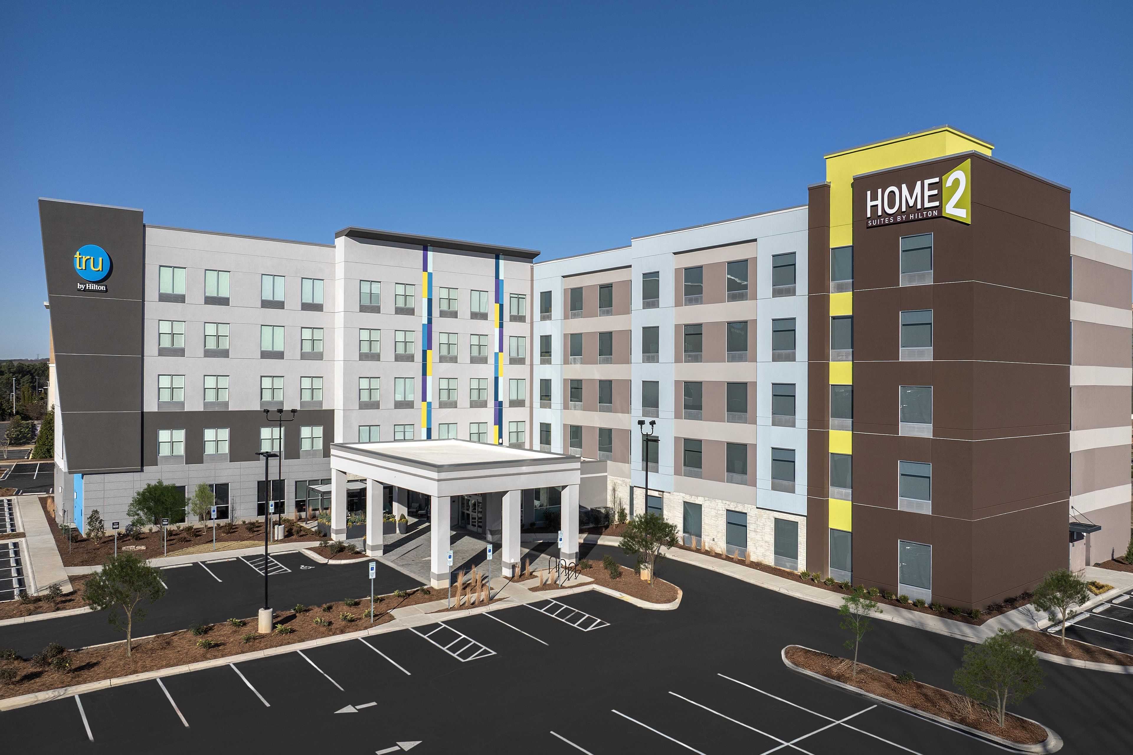 A modern hotel building with a central entrance, multiple floors, and a parking lot.