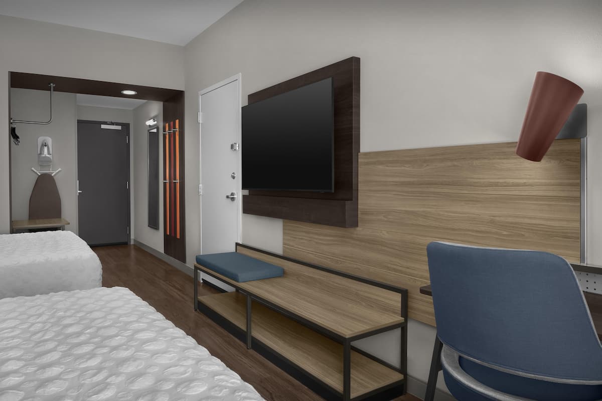 A modern hotel room with a large bed, a desk with a chair, a television mounted on the wall, and a shower area.