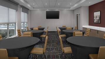 Sala de conferências com mesas e cadeiras redondas, uma TV de tela plana e vista para a cidade.
