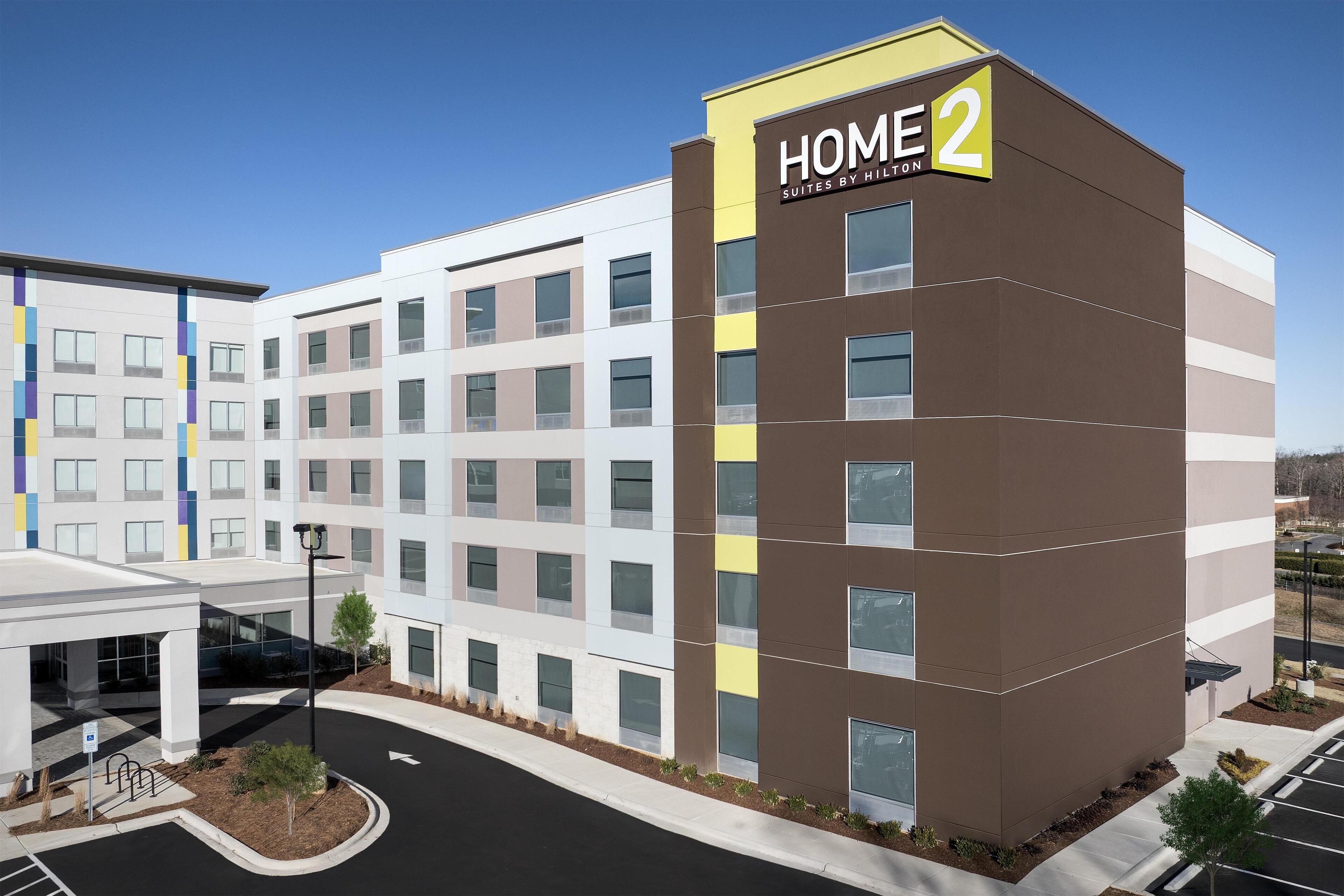 Un hotel de varios pisos con un diseño moderno, que presenta un llamativo letrero 'HOME 2' en la esquina.