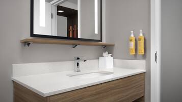 A modern bathroom with a white sink, wooden vanity, a mirror with a black frame, and two yellow soap dispensers on the wall.