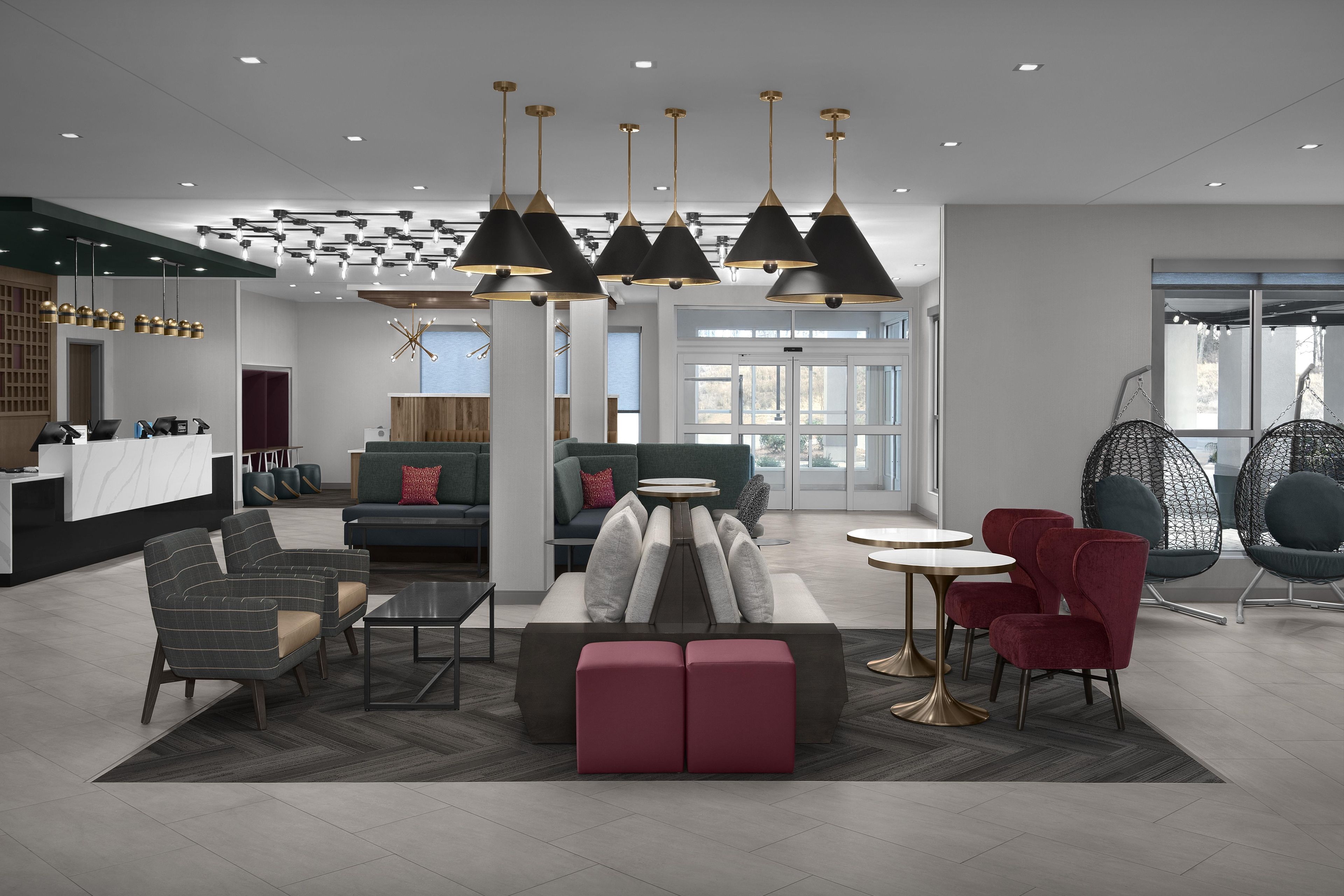 A modern hotel lobby with a reception desk, seating area, and large windows.