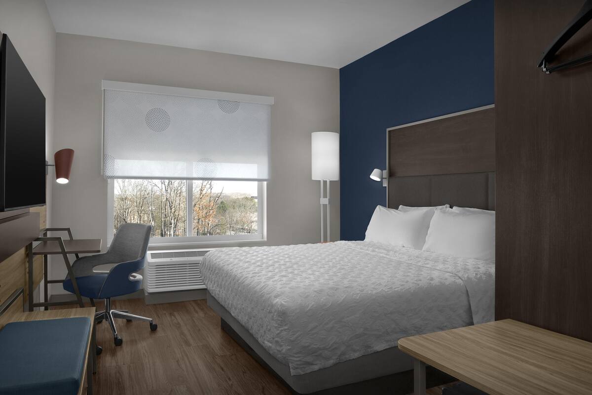 A modern hotel room with a large bed, a desk, a chair, and a TV.