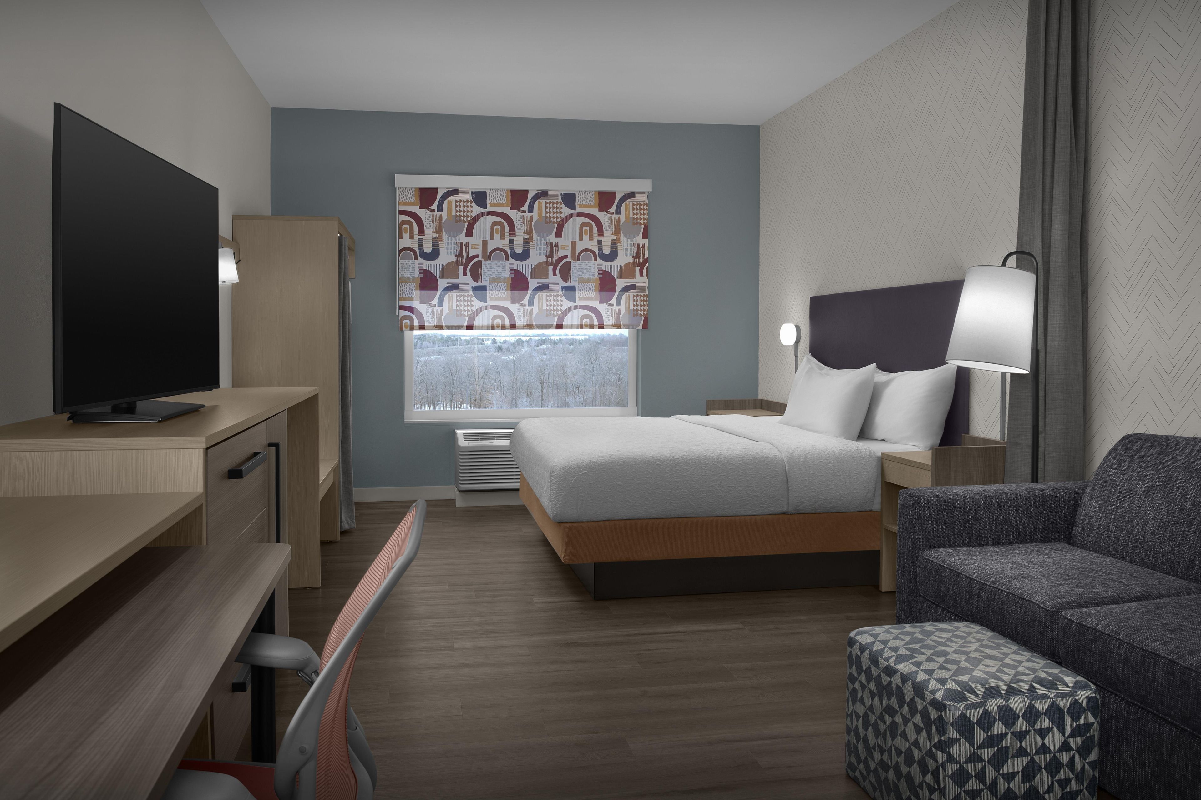 A hotel room with a bed, a desk, a TV, a chair, and a window with a view.