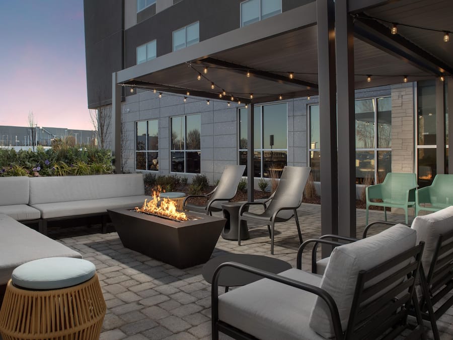 An outdoor seating area with a fire feature, lounge chairs, and a modern building in the background.