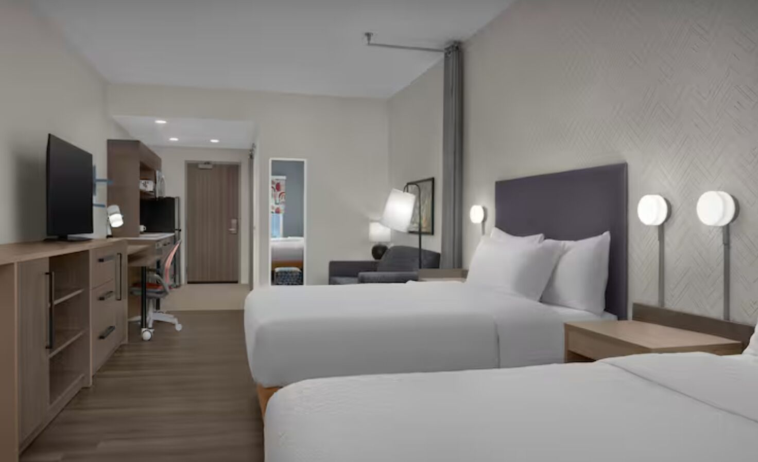 Habitación de hotel con dos camas, un escritorio, televisor y armario.