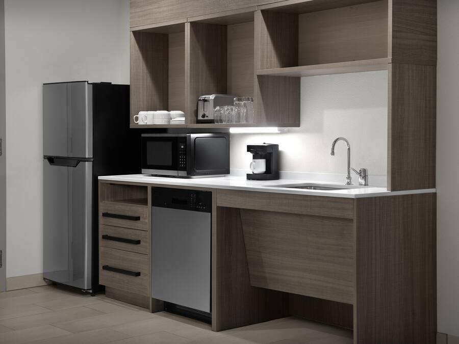 A compact kitchen with a refrigerator, microwave, coffee maker, and a dishwasher.