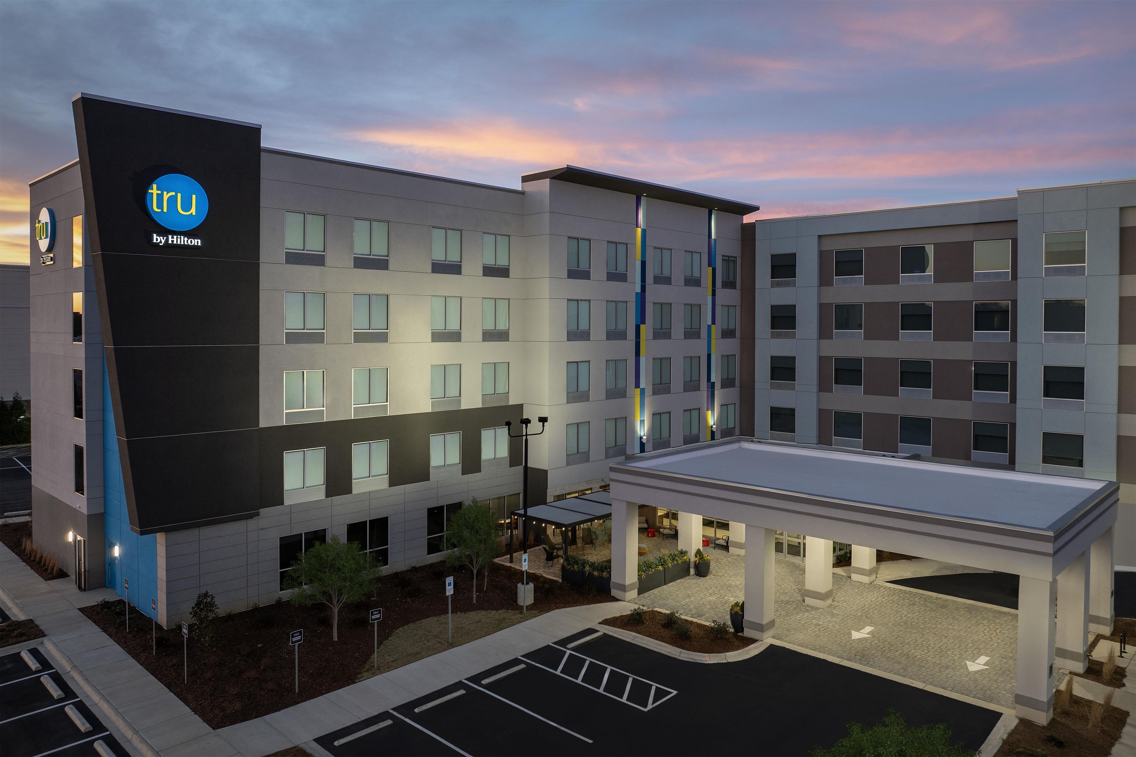 A modern hotel building with multiple floors, a covered outdoor area, and a parking lot.